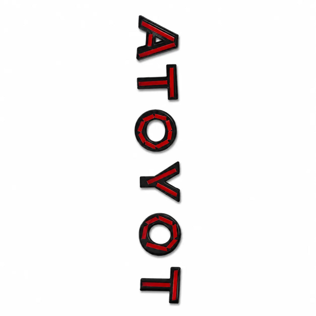 A vertical rectangular decal featuring the word 'ATOYOT' in bold red Tape with black lettering, shown on a plain white background.