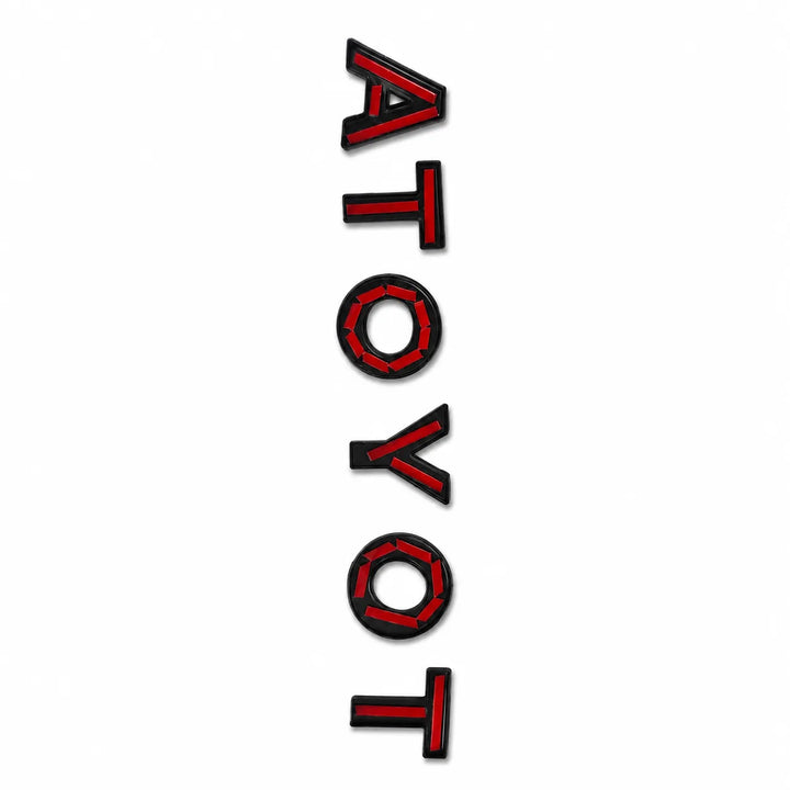 A vertical rectangular decal featuring the word 'ATOYOT' in bold red Tape with black lettering, shown on a plain white background.