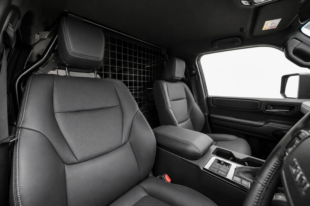 Front Seats passenger area of a Land Cruiser Toyota LC250 SUV, showing the front seats before the conversion and a rear mesh bulk head partition between the cargo area and the seats.