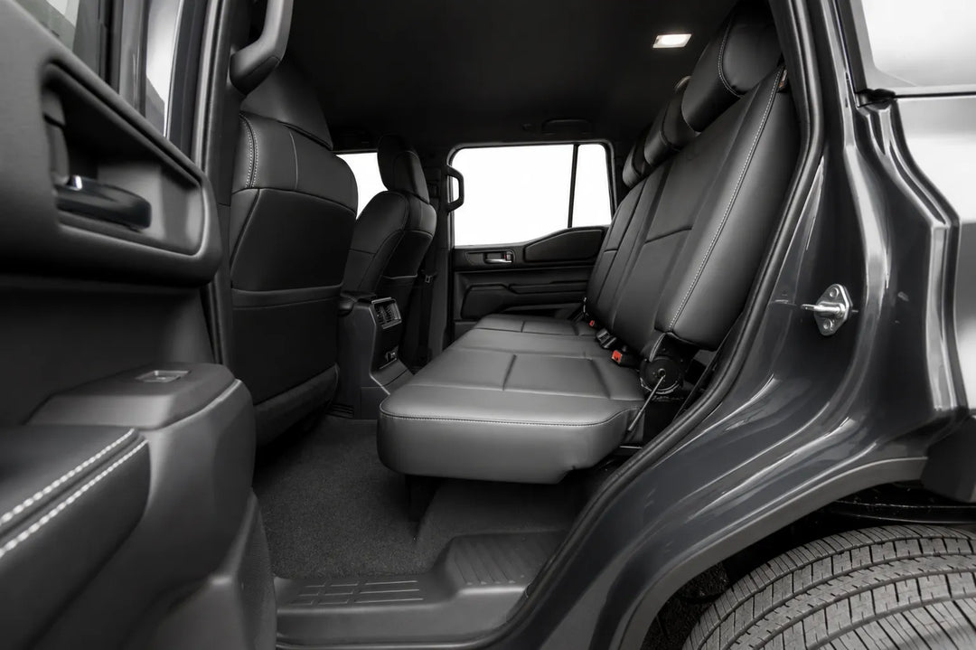Rear passenger area of a black vehicle after the conversion showing the folded-down center seat, rear bench seat conversion, door panel, carpet, and part of the tire.