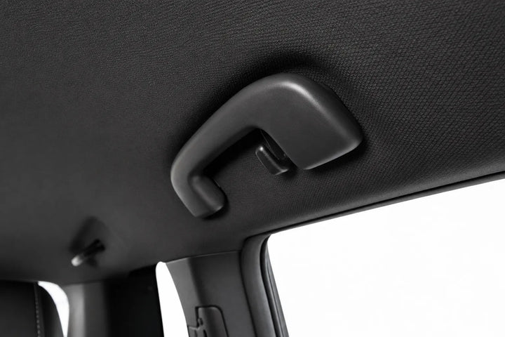 A close-up of a black plastic grab handle installed on a textured black car interior ceiling.
