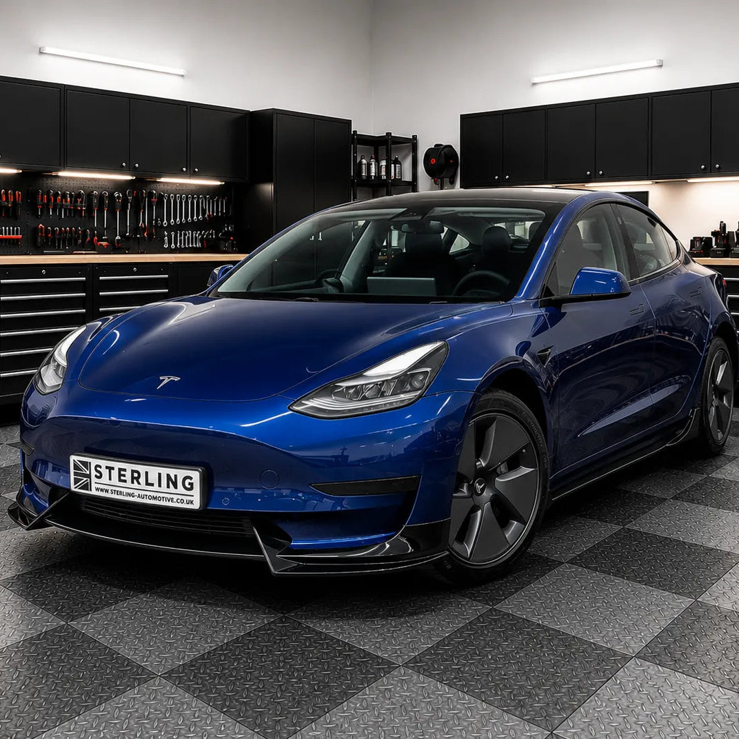 A metallic blue Tesla Model 3 parked inside the sterling workshop with black tool cabinets and a gray checkered floor. A license plate reading 'STERLING' is mounted on the front.