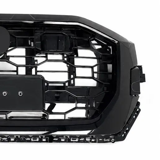 A close-up of a glossy black vehicle front grille with a honeycomb-style mesh pattern, photographed against a white background.