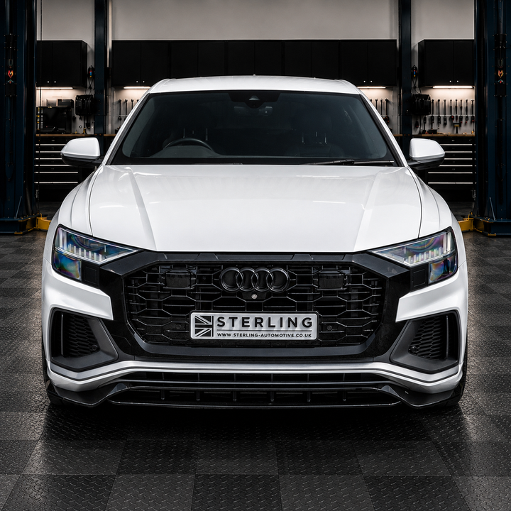 A white Audi Q8 parked facing forward in a garage setting, featuring a custom black rs style front grille with a central license plate that reads 'STERLING' and 'www.sterling-automotive.co.uk'