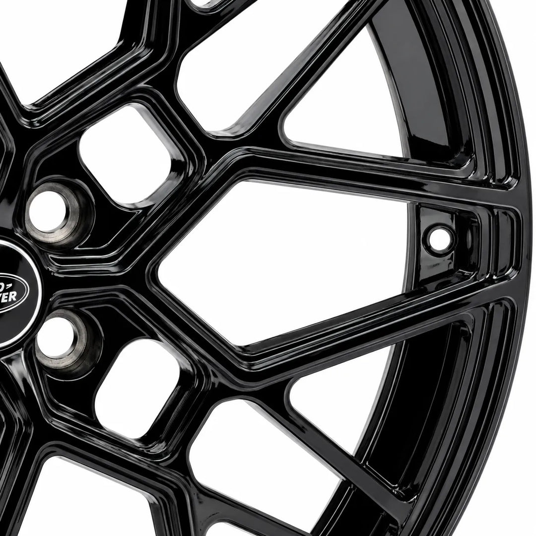 Close-up of a glossy black multi-spoke alloy wheel rim with a logo badge on the center cap, set against a plain white background.