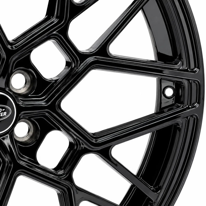 Close-up of a glossy black multi-spoke alloy wheel rim with a logo badge on the center cap, set against a plain white background.
