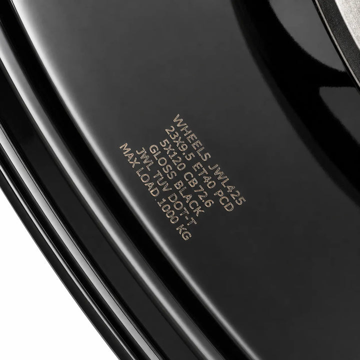 Close-up of a glossy black wheel rim with printed specifications on the side, including 'WHEELS JWL4.25 23x19.