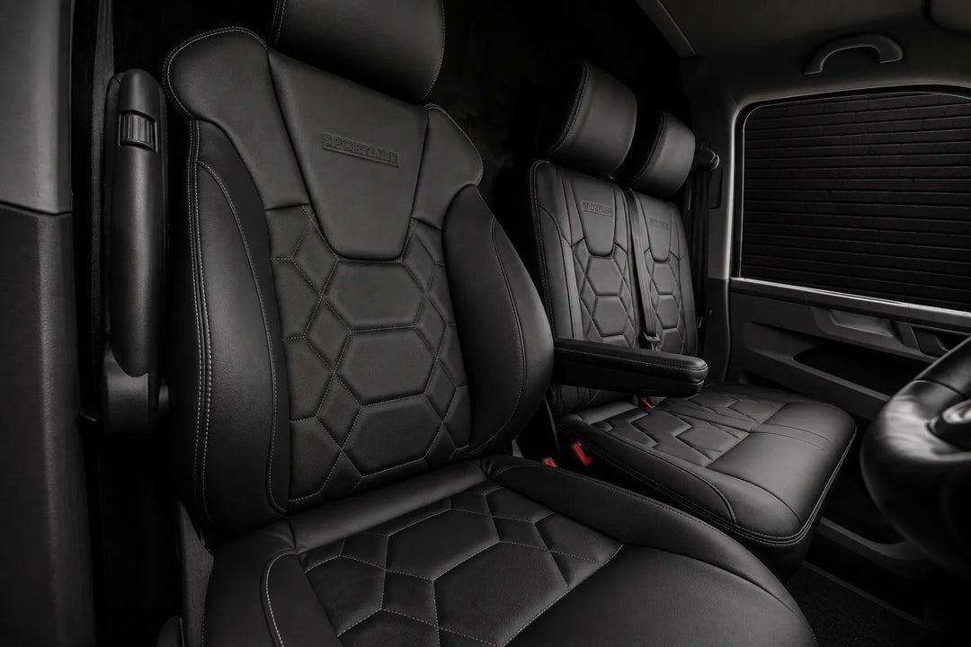 Black leather vehicle cabin seats with geometric hexagonal quilting and embossed branding on the headrests, shown inside a truck or SUV cab.