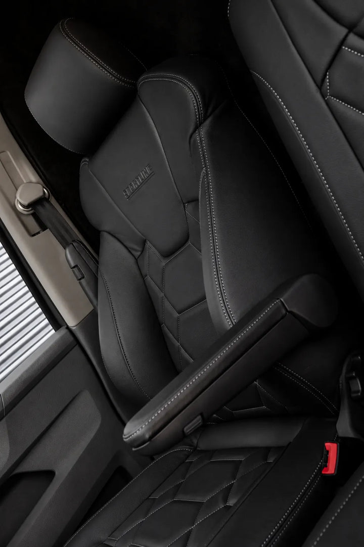 Close-up of a black leather car seat with diamond-quilted stitching, a matching center console armrest, and a visible seatbelt buckle area inside a vehicle cabin.