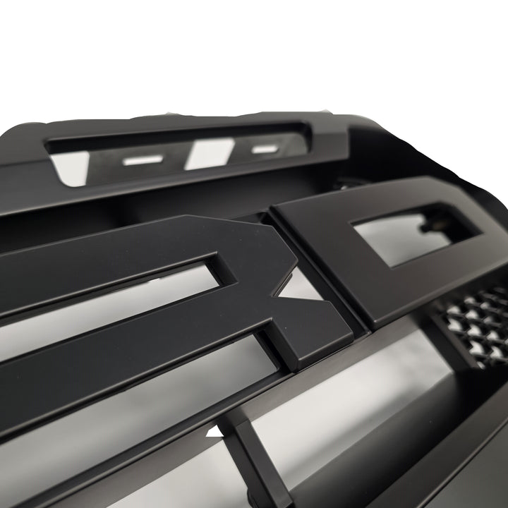 Close-up of a black metal front grille with a slatted design and cutouts, shown against a white background.