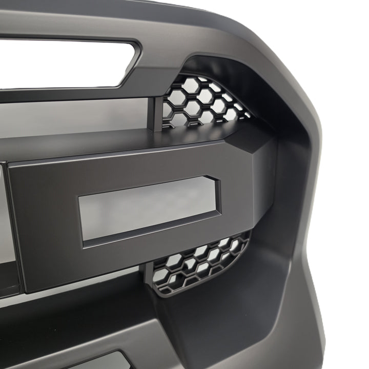 Close-up of a matte black truck grille insert with honeycomb mesh accents and a blank rectangular badge area, shown against a white background.