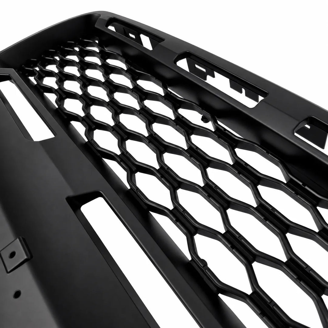 A close-up of a black honeycomb-style front grille insert with cutouts, shown on a plain white background.