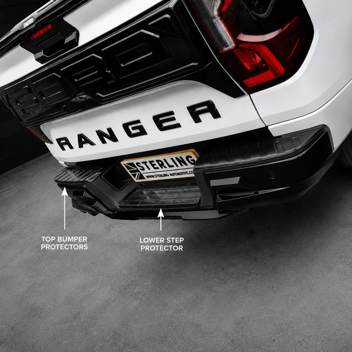 Black truck bumper protectors shown installed on the rear of a white Ford Ranger, with labeled callouts for top bumper protectors and lower step protector. The truck is photographed in a studio setting on a gray floor.