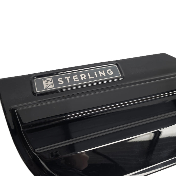 Close-up of a glossy black plastic component featuring a silver rectangular badge with the word 'STERLING' and a small geometric logo, photographed against a white background.