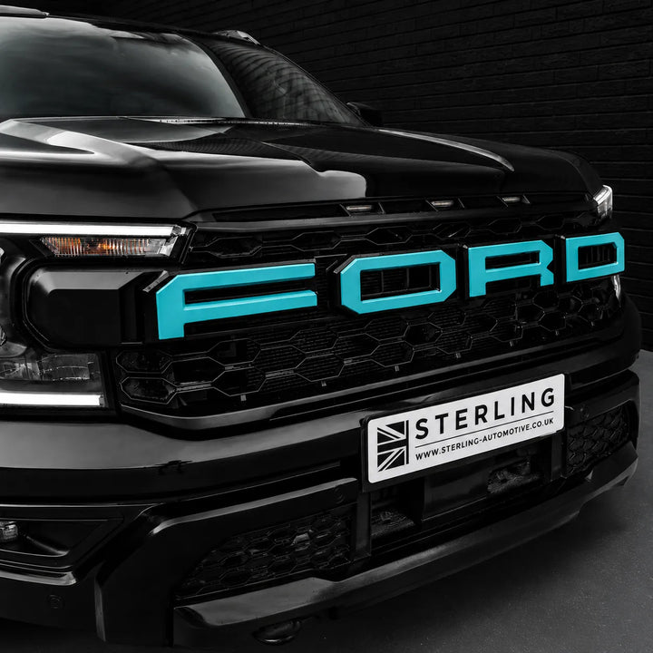 A close-up of the front grille of a black Ford vehicle, featuring bright turquoise blue 'FORD' lettering on the grille and a white 'STERLING' license plate holder below.
