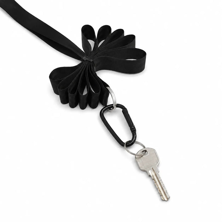 A black fabric keychain organizer with a looped ribbon design, attached to a black carabiner holding a silver key, shown on a plain white background.
