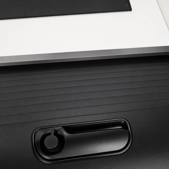 Close-up of a black textured panel with an integrated recessed handle or slot, set against a white surface with a dark strip at the top.