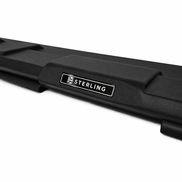 A close-up shot of a Sterling Design Style rear tailgate spoiler finished in black textured plastic with a silver and black Sterling brand label on its rear, against a plain white background.