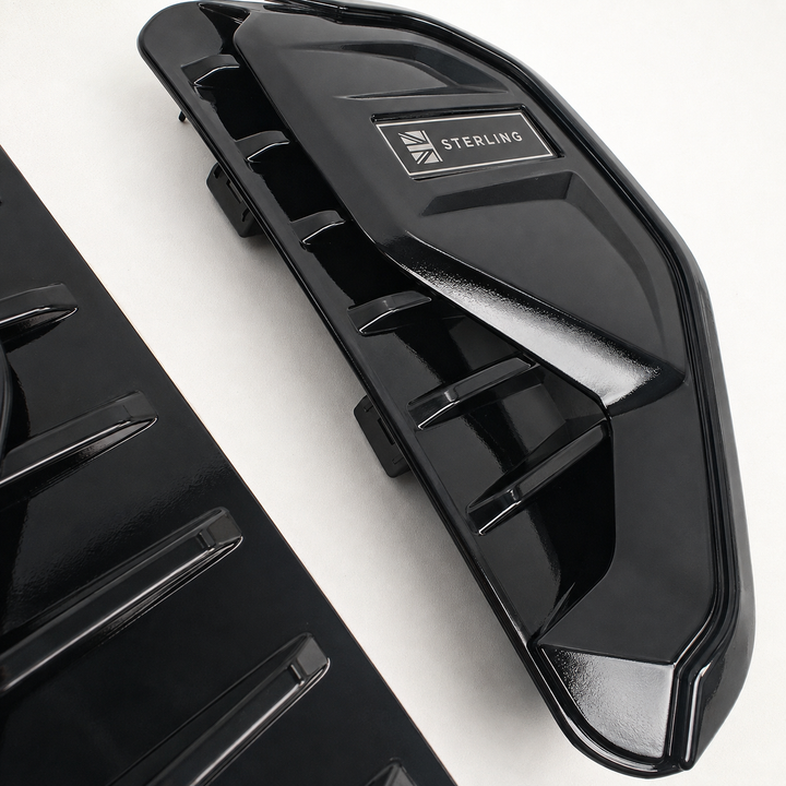 A glossy black molded plastic automotive part with a visible STERLING logo badge, photographed on a clean white background with another matching part partially visible at the lower left.