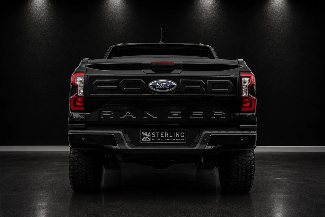 Rear view of a black Ford Ranger pickup truck in a dark studio setting, with the Ford logo and Ranger lettering visible on the tailgate and a Sterling badge on the license plate area.