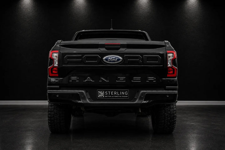 Rear view of a black Ford Ranger pickup truck in a dark studio setting, with the Ford logo and Ranger lettering visible on the tailgate and a Sterling badge on the license plate area.