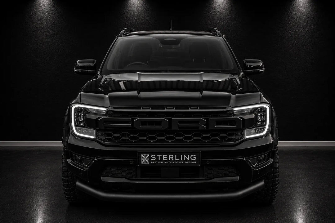 A black Ford Ranger pickup truck shown from the front in a dark studio setting, with a prominent black front grille featuring embossed 'FORD' lettering and a 'STERLING' badge on the lower bumper area.