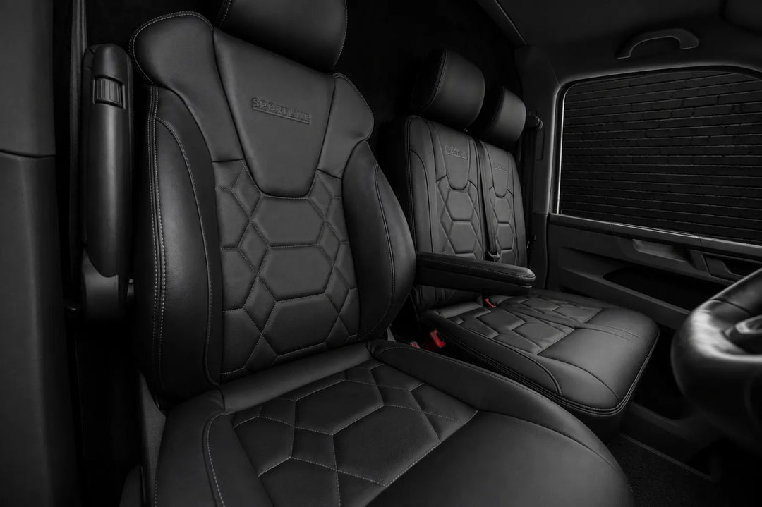 Black leather vehicle front seats with quilted hexagonal stitching and a small embossed logo on the headrests, shown inside a vehicle cabin.