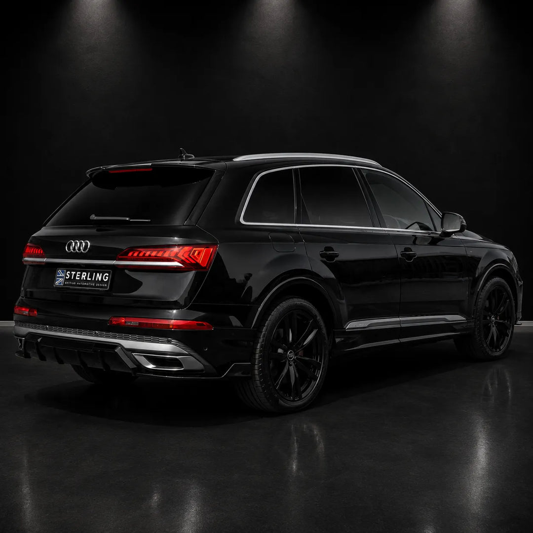 A black Audi Q7 SUV shown from a rear three-quarter angle in a dark studio setting with spotlighting. The vehicle features a custom dark tinted glass roof, black wheels, and a license plate frame with the brand name 'STERLING'.