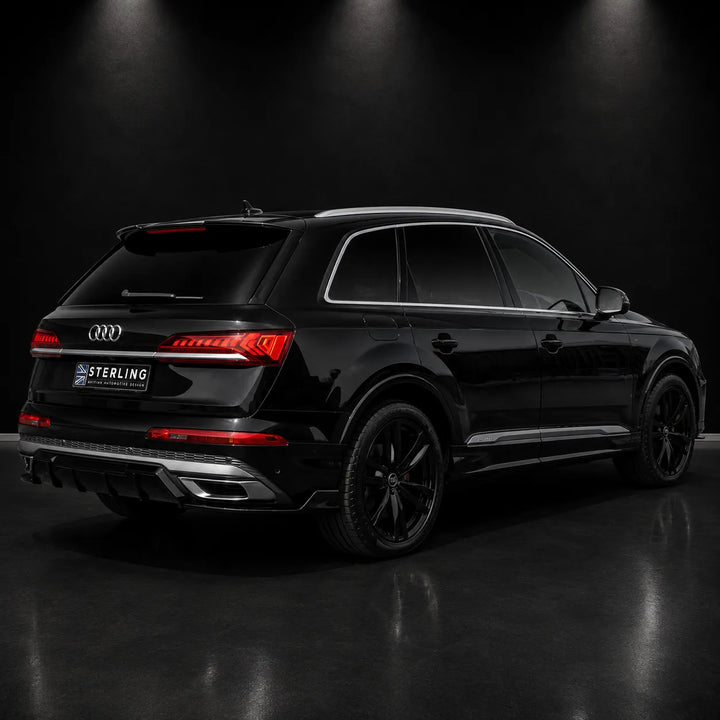 A black Audi Q7 SUV shown from a rear three-quarter angle in a dark studio setting with spotlighting. The vehicle features a custom dark tinted glass roof, black wheels, and a license plate frame with the brand name 'STERLING'.