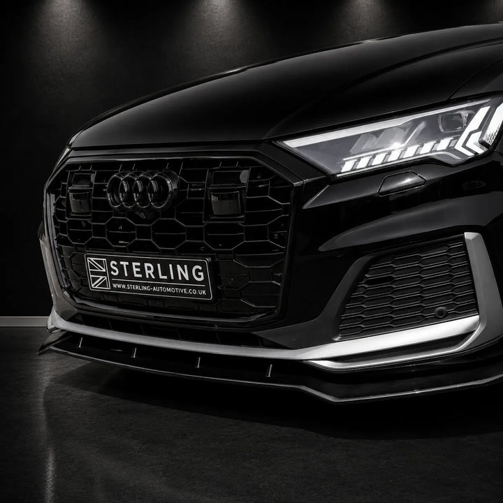 Close-up of the front grille and lower bumper area of a black Audi, showing a branded Sterling automotive grille insert and license plate frame. The car is photographed in a dark studio setting with dramatic lighting.