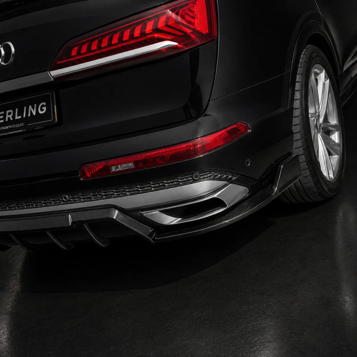 Close-up rear three-quarter view of a black Audi vehicle showing the rear bumper, diffuser, exhaust outlets, taillight, and wheel on a dark studio floor.