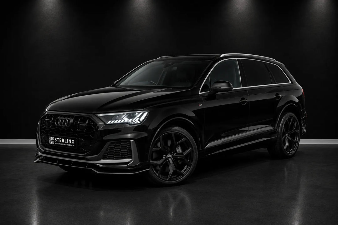 A black Audi Q7 SUV with custom dark gray and black Sterling body kit elements, shown from a three-quarter front angle in a dark studio setting.