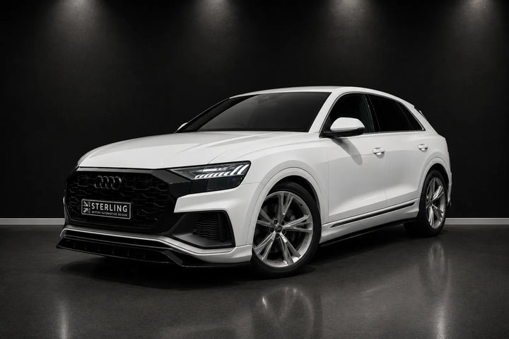 A white Audi Q8 SUV with a custom black front grille and a 'STERLING' license plate, photographed in a dark studio setting with a reflective floor.