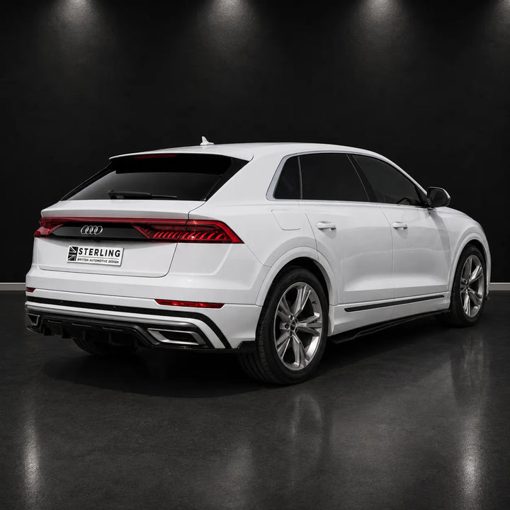 A white Audi Q8 SUV photographed from the rear three-quarter angle in a dark studio setting with a reflective floor. The license plate reads STERLING, indicating the visible brand.