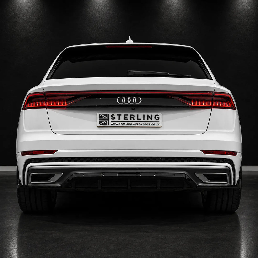 Rear view of a white Audi station wagon with a black diffuser and a central license plate frame reading STERLING, photographed in a dark studio setting.