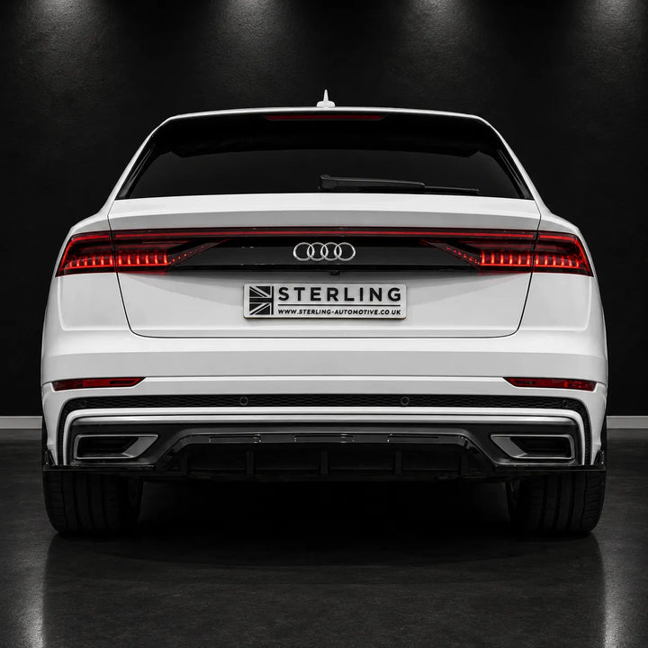 Rear view of a white Audi station wagon with a black diffuser and a central license plate frame reading STERLING, photographed in a dark studio setting.