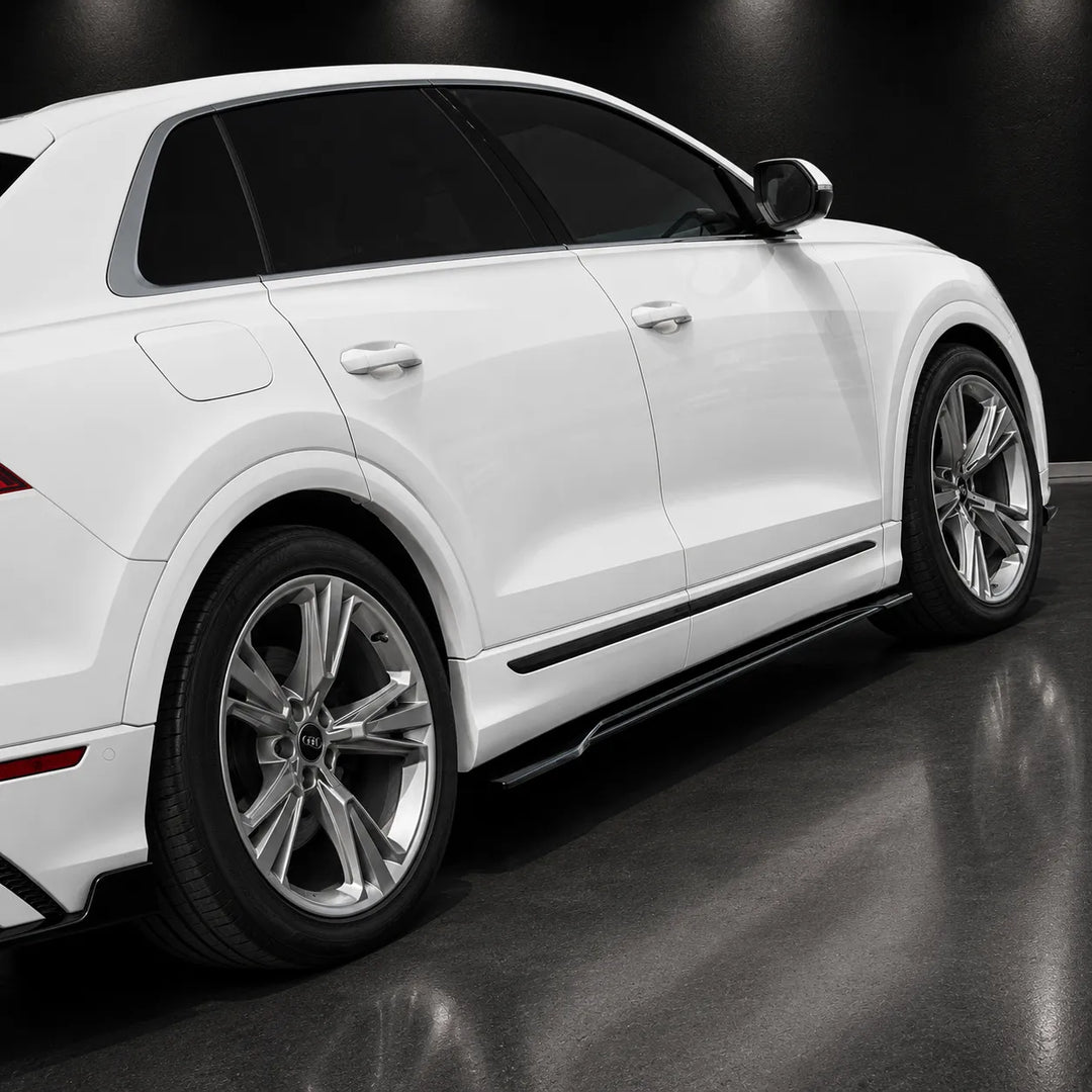 A white SUV shown from a rear three-quarter angle in a dark studio setting, highlighting the side profile, wheels, and black side skirts.