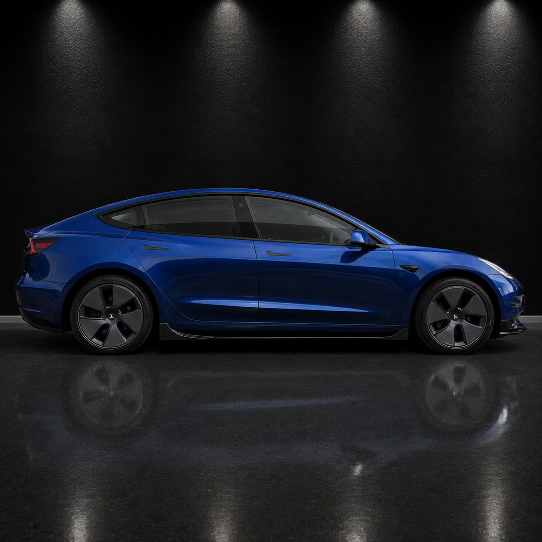 A blue Tesla Model Y sedan shown in a side profile view, parked on a dark reflective floor under spotlighting against a black background.
