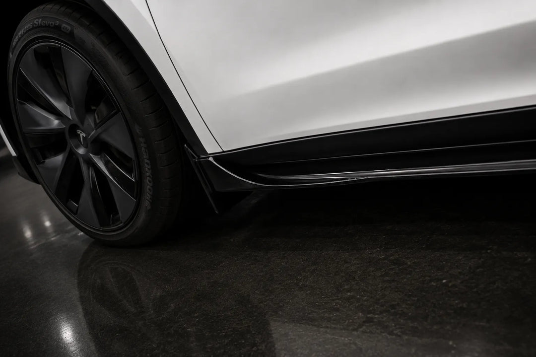 Close-up of the lower side of a white vehicle showing a black wheel, side skirt, and dark floor.