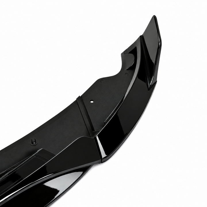 A glossy black automotive lower splitter part, gloss lip trim piece, shown at an angle on a plain white background.