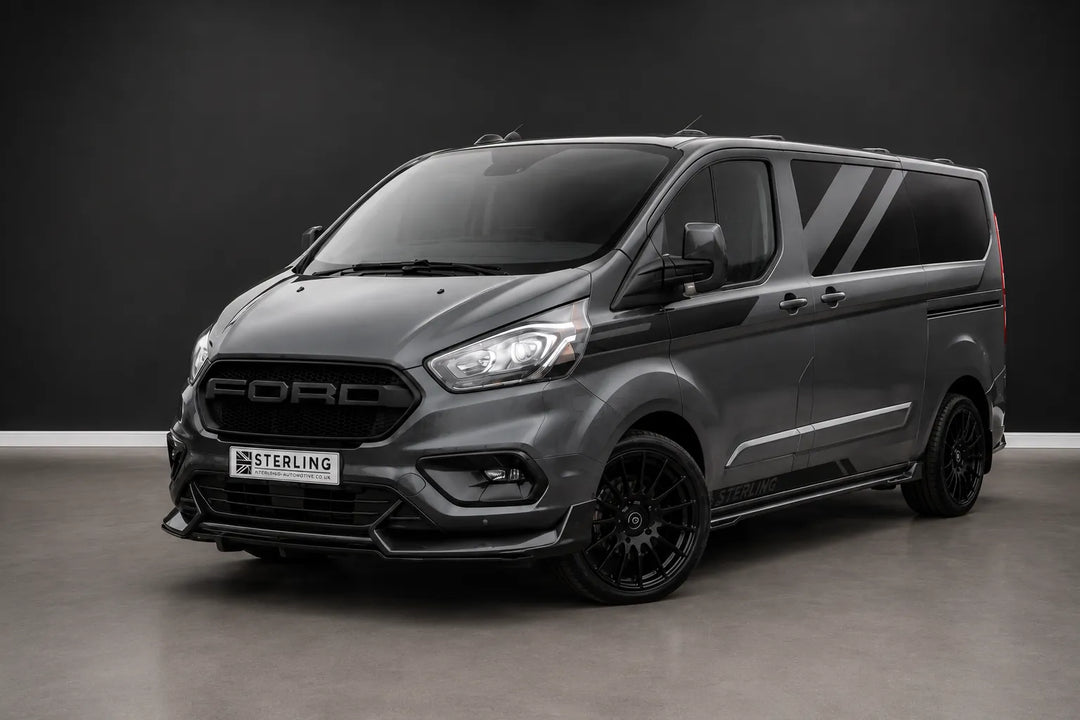A dark gray customized Ford Transit van with black wheels and a front lip spoiler, photographed in a studio setting with a dark gray background.