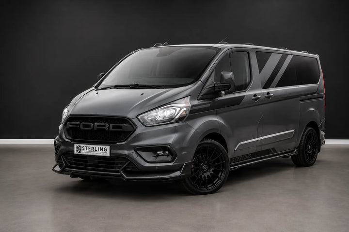 A dark gray customized Ford Transit van with black wheels and a front lip spoiler, photographed in a studio setting with a dark gray background.