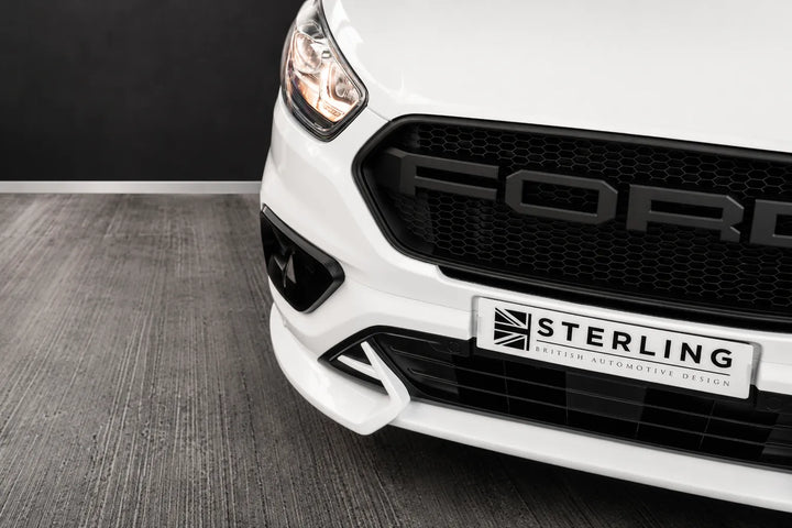Close-up of the front bumper and grille of a white Ford vehicle, showing a black honeycomb grille with a silver Ford logo, a white Sterling badge, and a gray textured floor.