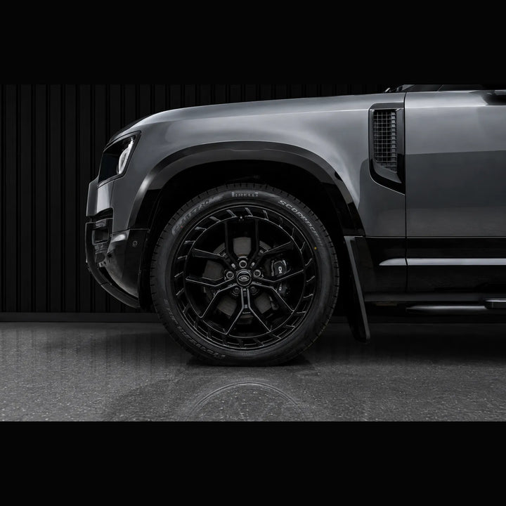 Close-up of a dark gray SUV wheel and fender area, showing a black multi-spoke alloy tire with visible 'BFGoodrich' lettering on the sidewall, photographed in a dark studio setting.